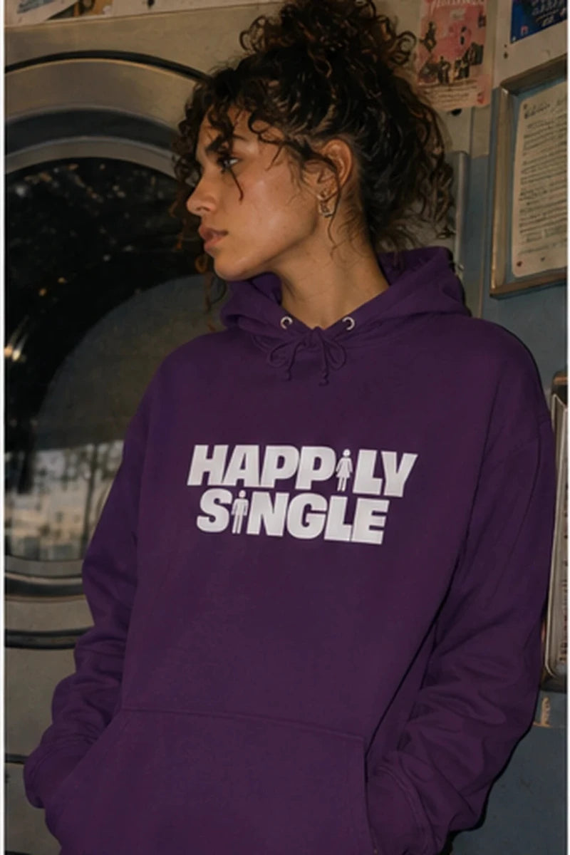 Gen Z woman wearing purple Happily Single hoodie in cinematic laundromat setting