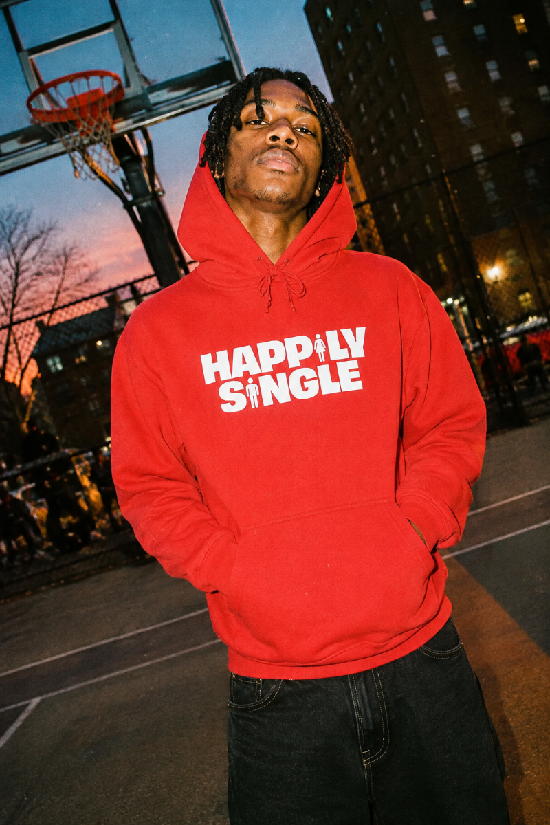 Gen Z man wearing red Happily Single hoodie on outdoor basketball court at dusk