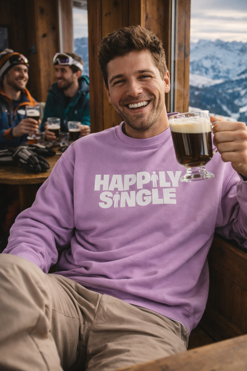 Man wearing a lavender 'Happily Single' sweatshirt at a mountain lodge with others in the background.