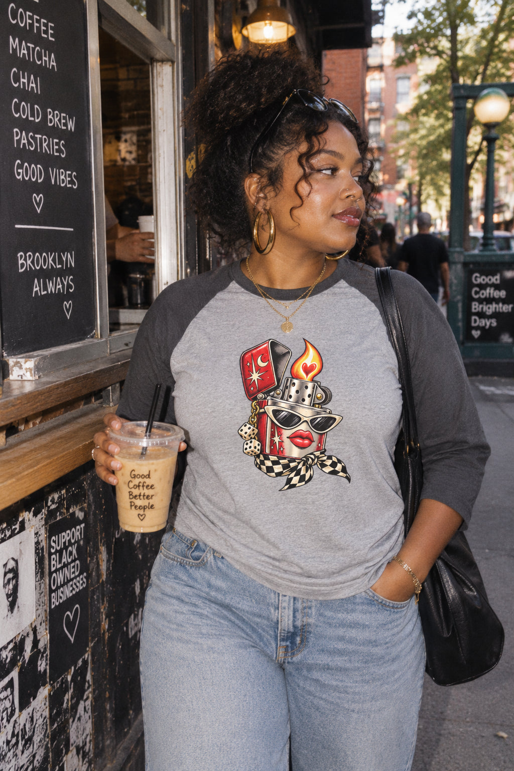 Woman wearing a heather gray and charcoal Heartstarter raglan T-shirt while holding iced coffee outside an urban coffee shop.