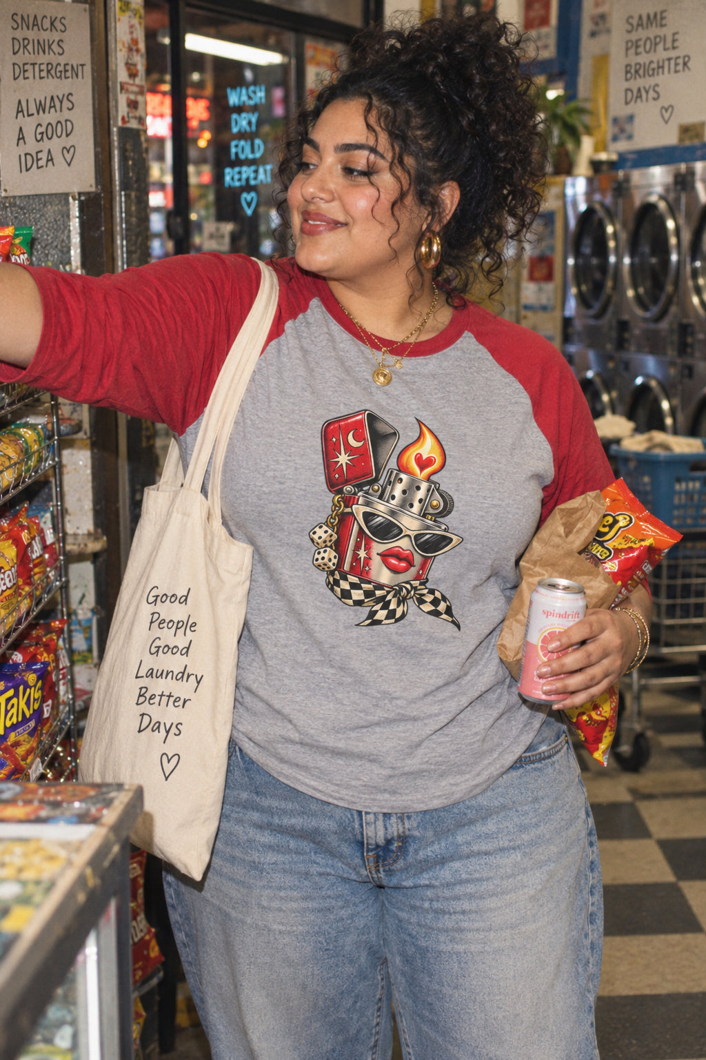 Woman wearing the Heartstarter gray and red raglan baseball tee featuring a retro lighter illustration while shopping for snacks at a laundromat.
