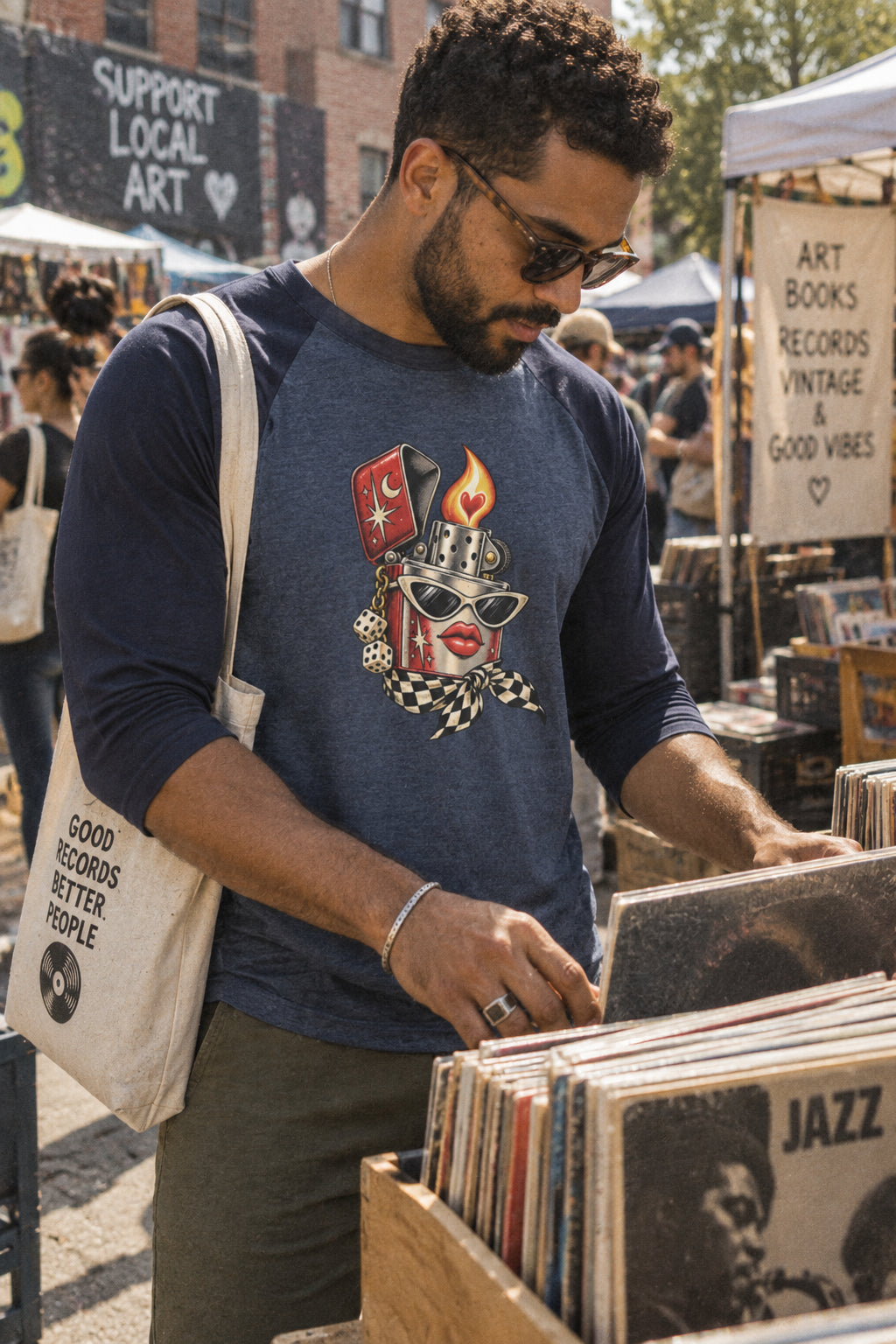 Man wearing the heather navy Heartstarter lighter graphic baseball shirt while browsing records at an outdoor vintage market.