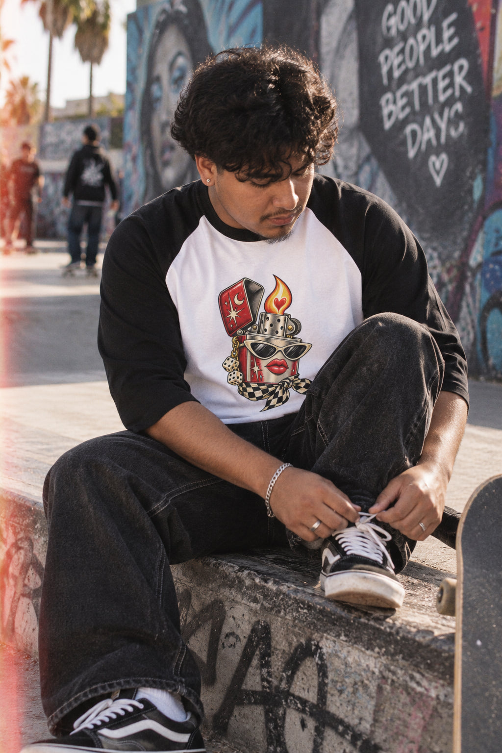 Young man wearing the white and black Heartstarter lighter graphic baseball tee while tying his sneakers at an urban skatepark.