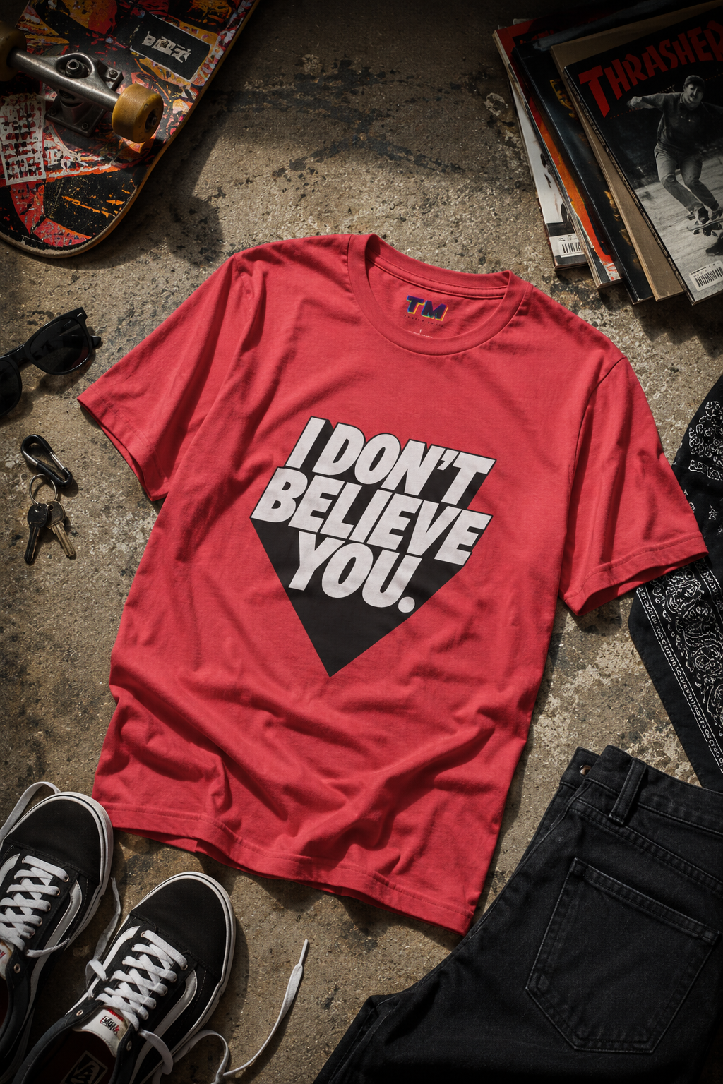 Flat-lay product photography of the I Don't Believe You unisex graphic t-shirt in red surrounded by casual accessories on a dark textured background.