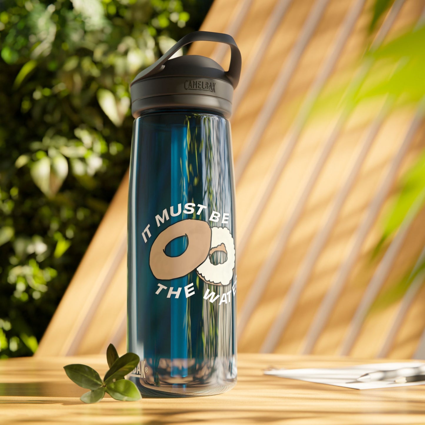 It Must Be The Water Bottle 25oz blue reusable water bottle with donut bagel humor design in outdoor sunlight lifestyle scene