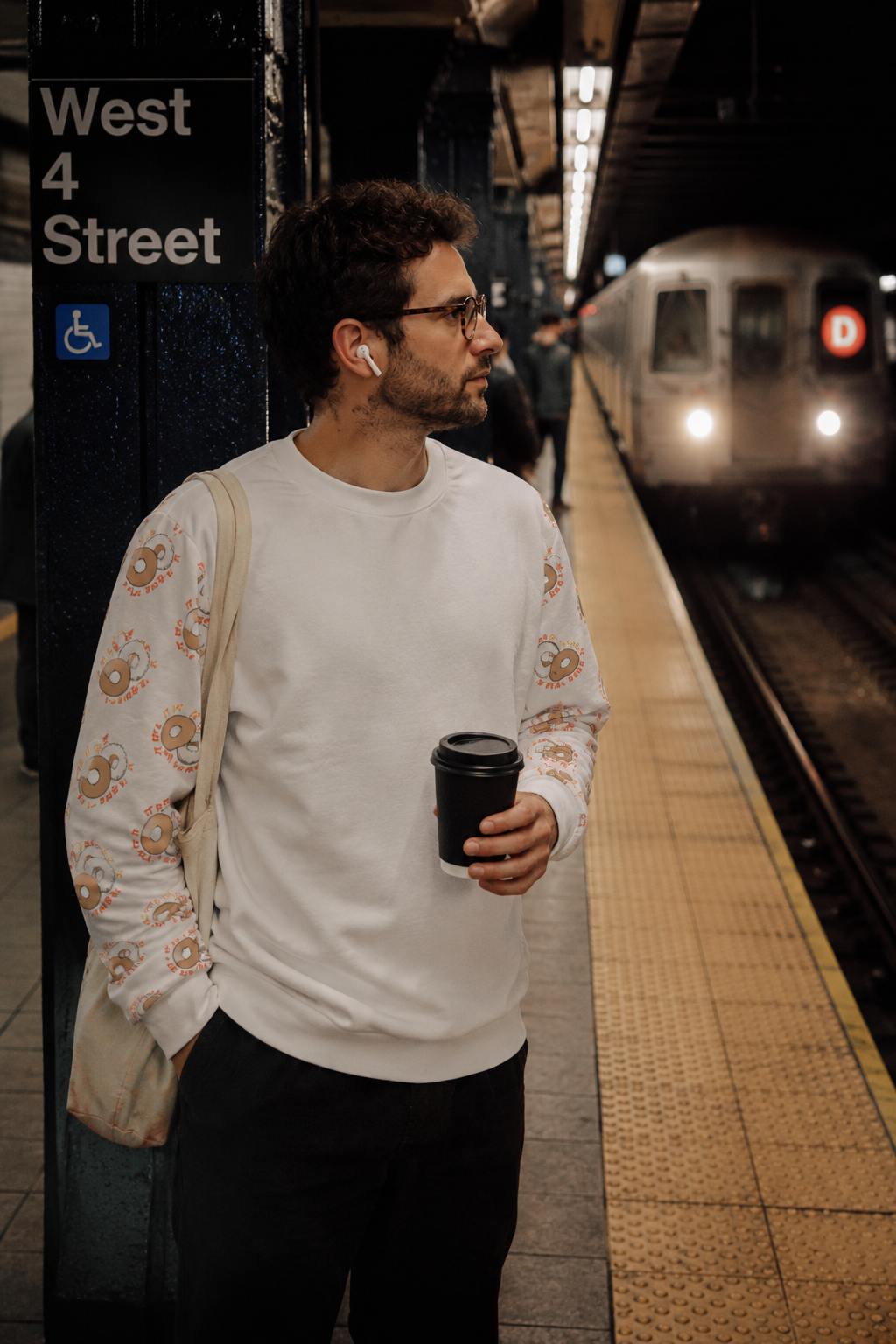 Millennial man wearing It Must Be The Water sweatshirt at West 4th Street subway station in NYC