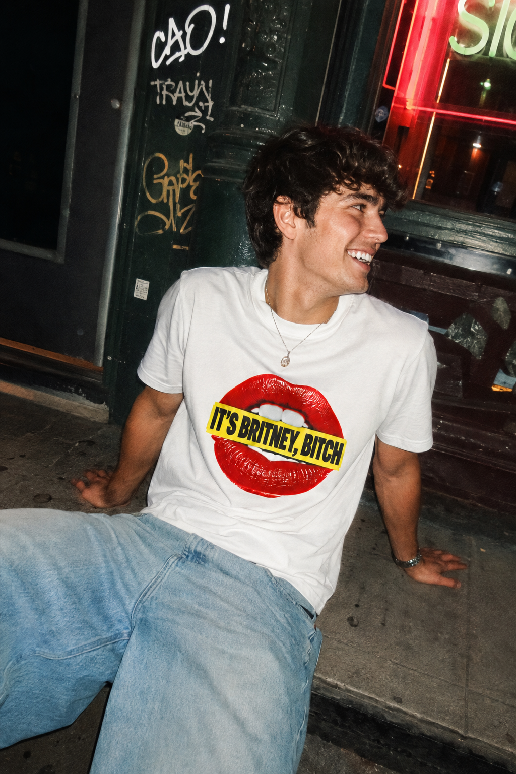 Male Gen Z wearing the It’s Britney, Bitch Britney Spears homage graphic T-shirt in a candid nighttime street scene.