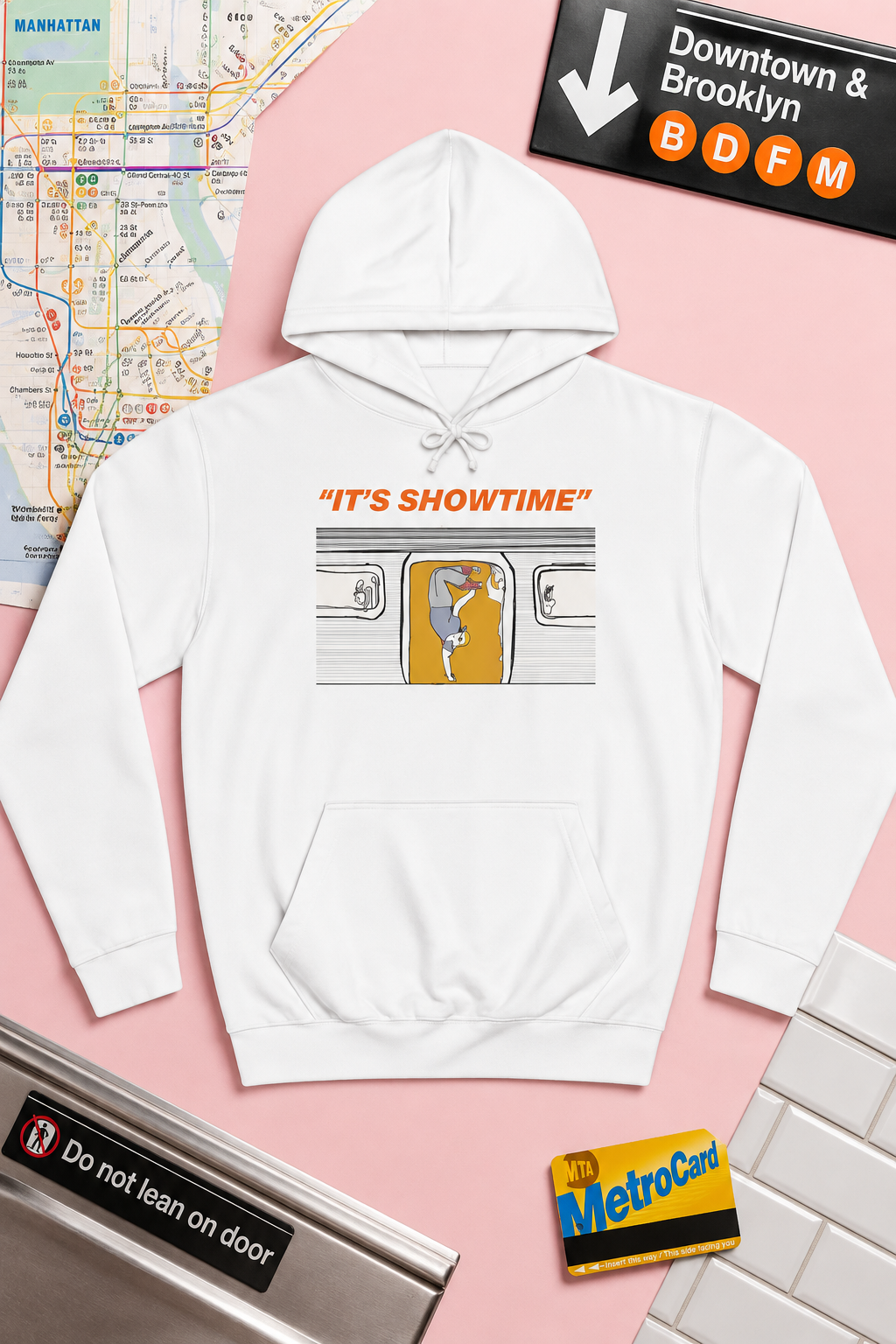 White It’s Showtime graphic hoodie flat lay on a pastel pink background with New York City subway-inspired details