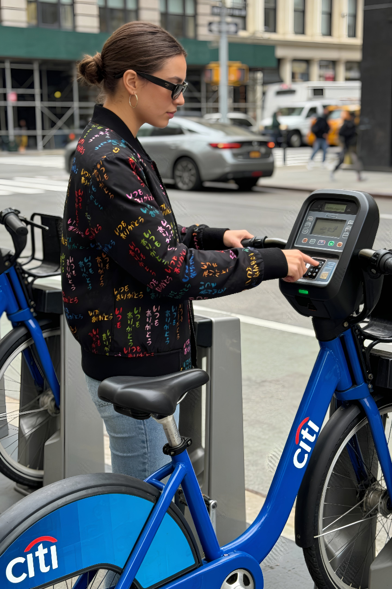 Woman wearing Japanese Street Art Unisex Bomber Jacket beside a Citi Bike in New York City.