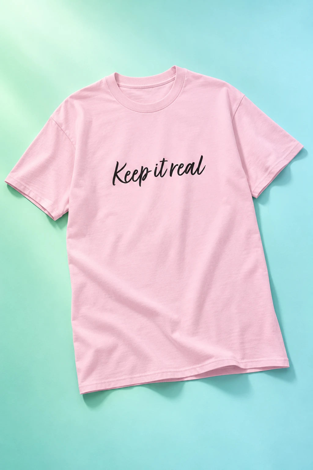 Tantrum Media light pink Keep It Real T-Shirt with black script lettering on a mint and aqua gradient background.