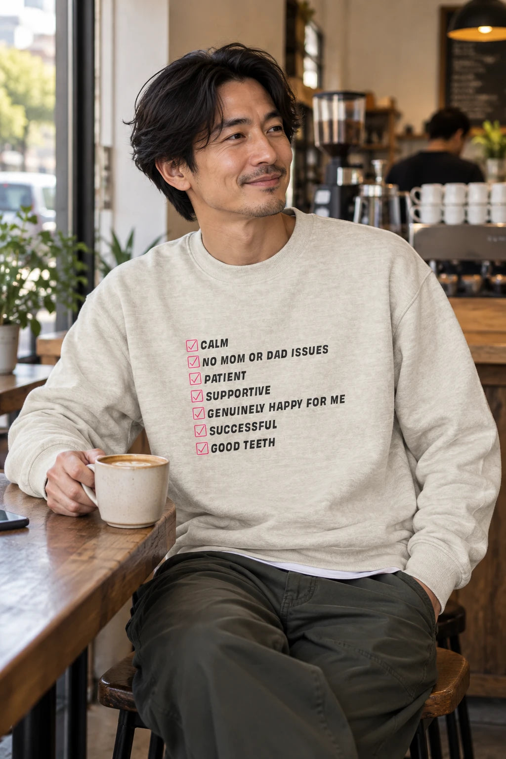 Oatmeal Kim Kardashian’s Men’s Must-Have List crewneck sweatshirt on a man sitting in a cafe holding a coffee.