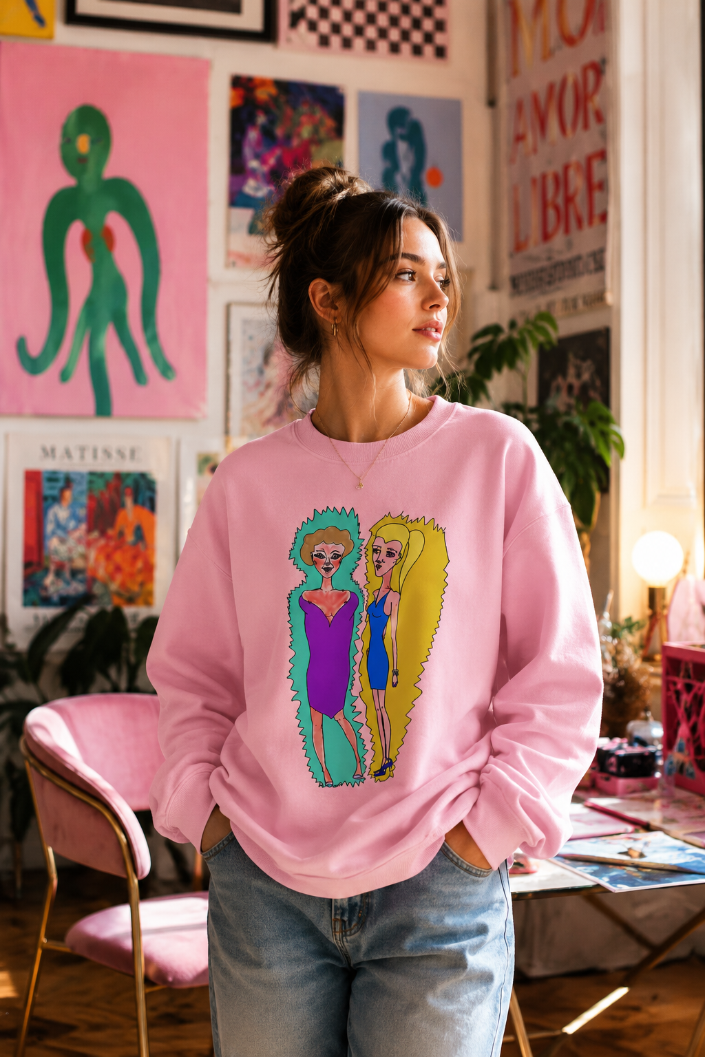 Female wearing Lads Unisex Graphic Sweatshirt featuring original hand-drawn character artwork in a colorful creative studio setting.