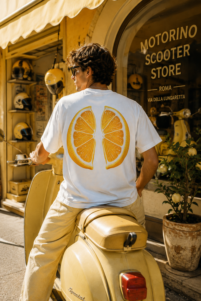 Male wearing white lemon back print T-shirt on a vintage yellow scooter in a European street scene