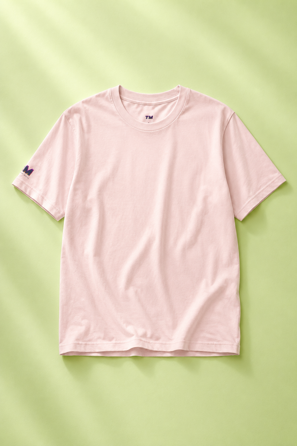 Editorial flat lay of a light pink cotton T-shirt on a green background.
