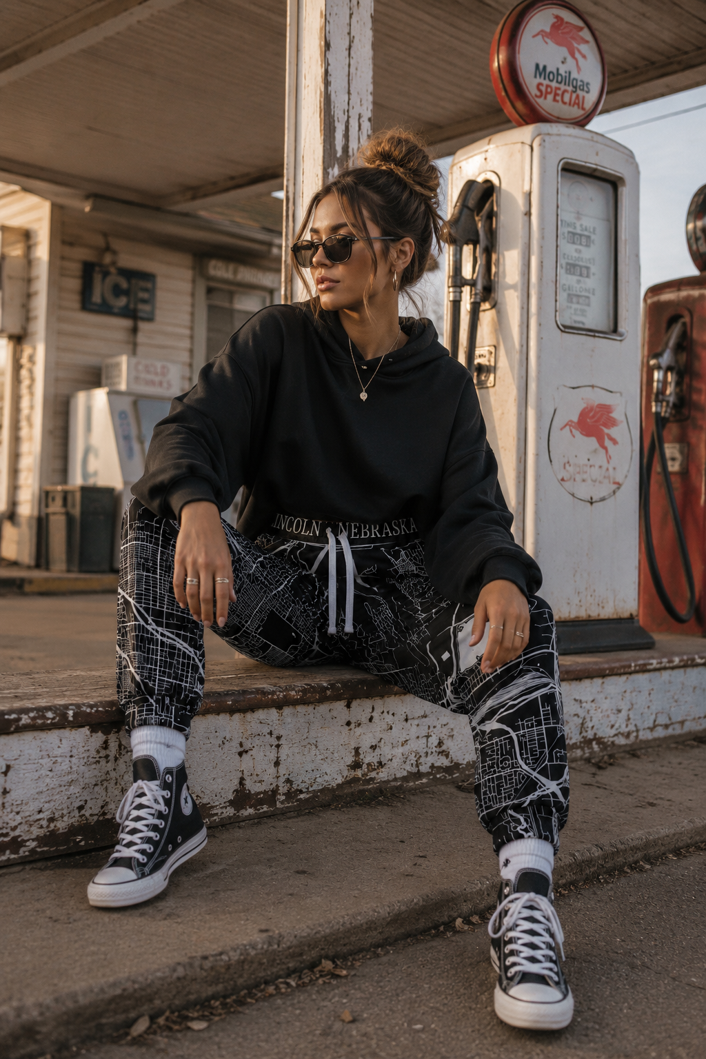 Gen Z model wearing Lincoln Nebraska map joggers outside a vintage gas station in a cinematic editorial streetwear photoshoot.