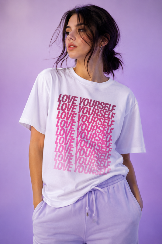 Woman wearing the Love Yourself graphic unisex T-shirt in white with bold pink typography in a casual lifestyle portrait.