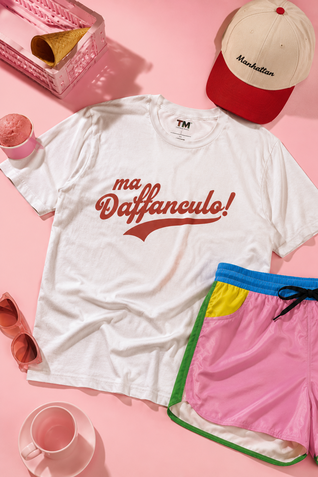 White Ma Vaffanculo graphic t-shirt flat lay with matching cap on a pastel pink background.