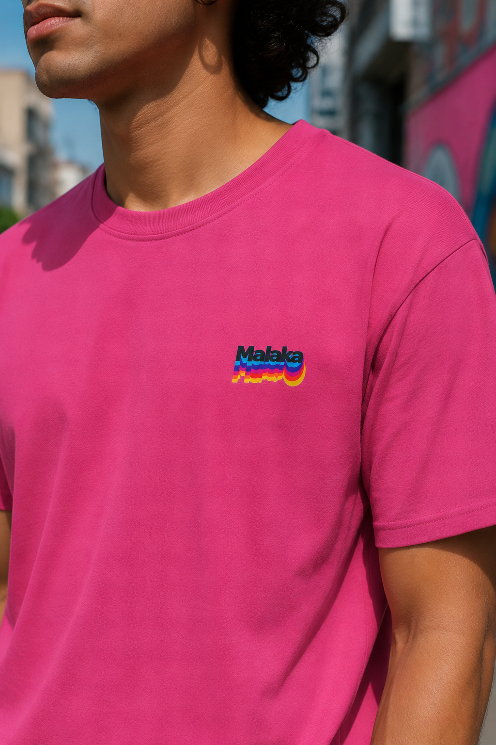 Man wearing a pink Malaka Greek slang T-shirt with a colorful left chest graphic outdoors, close-up view