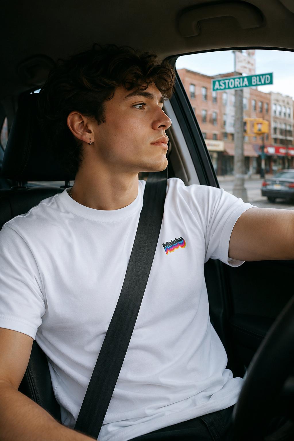 Gen Z man wearing a white Malaka Greek slang T-shirt while driving through Astoria, Queens