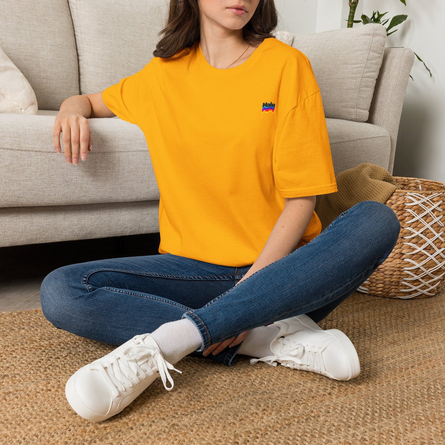 Woman wearing a yellow Malaka Greek slang T-shirt while seated indoors in a casual lifestyle scene