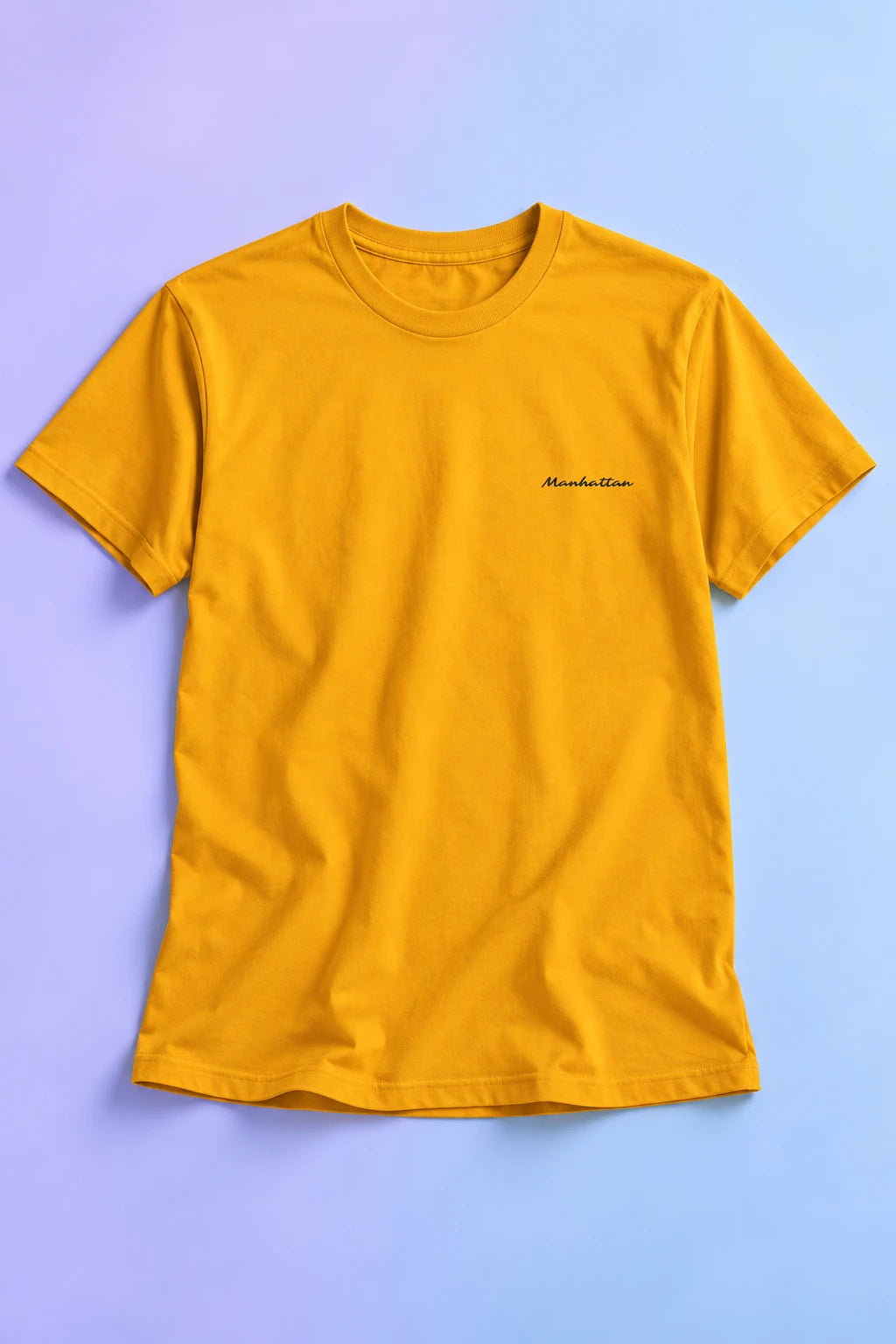 Yellow Manhattan T-shirt laid flat on a pastel lavender and blue gradient background.