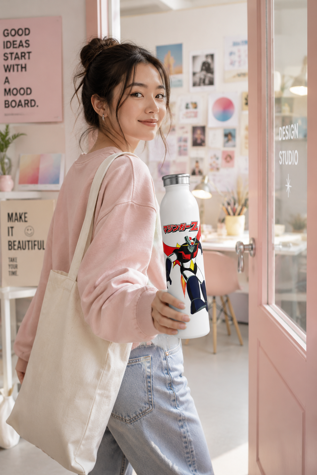 Gen Z woman carrying a Mazinger Z water bottle into a pastel-colored graphic design studio.