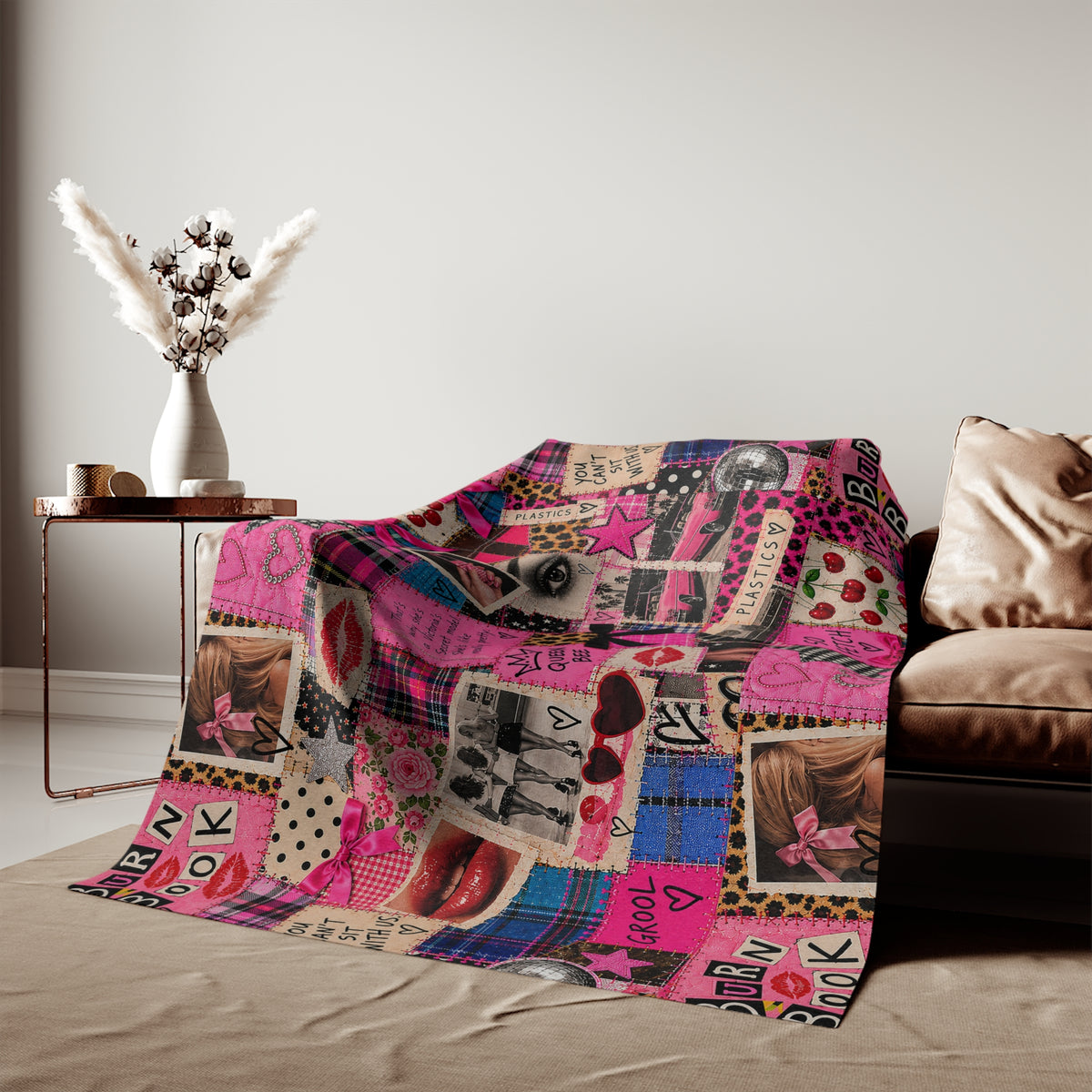 Tantrum Media Regina George Burn Book Sweatshirt Blanket draped over a beige sofa, adding colorful pink retro movie-inspired decor to a living room.