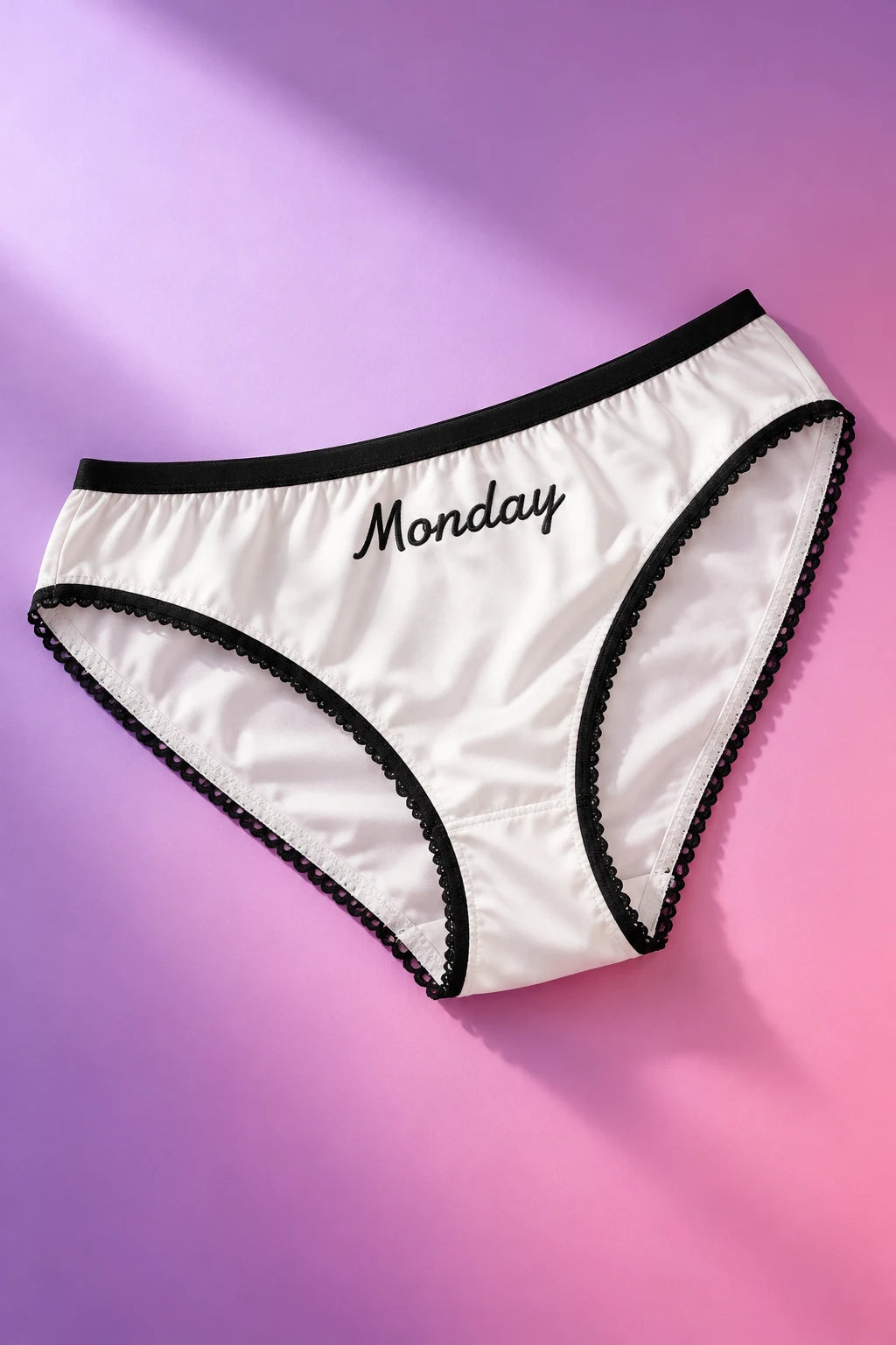 Tantrum Media Monday Panty in white with black trim and Monday script, laid flat on a purple and pink gradient background.