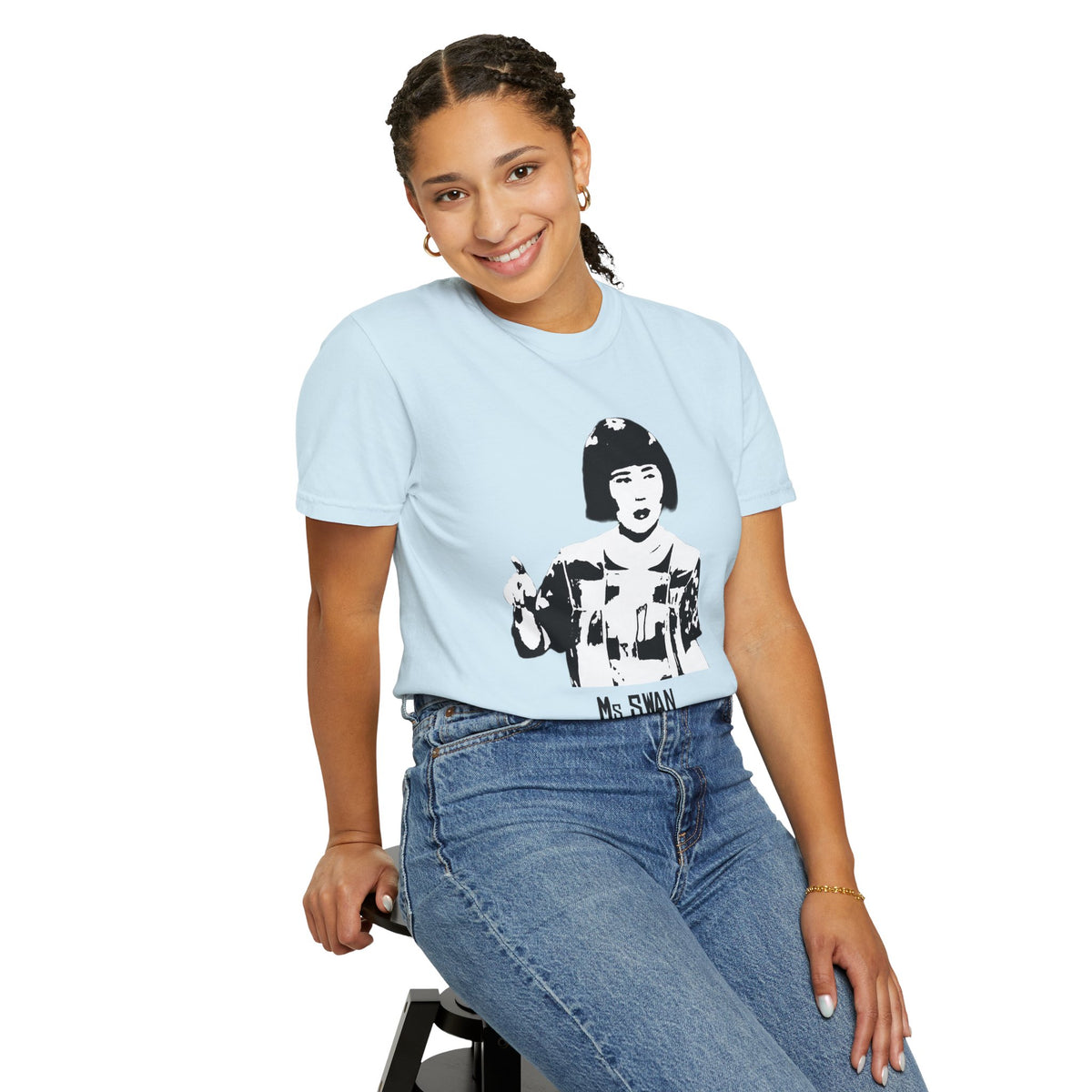 Seated model wearing a light blue Tantrum Media Ms Swan graphic T-shirt and jeans against a white studio background.