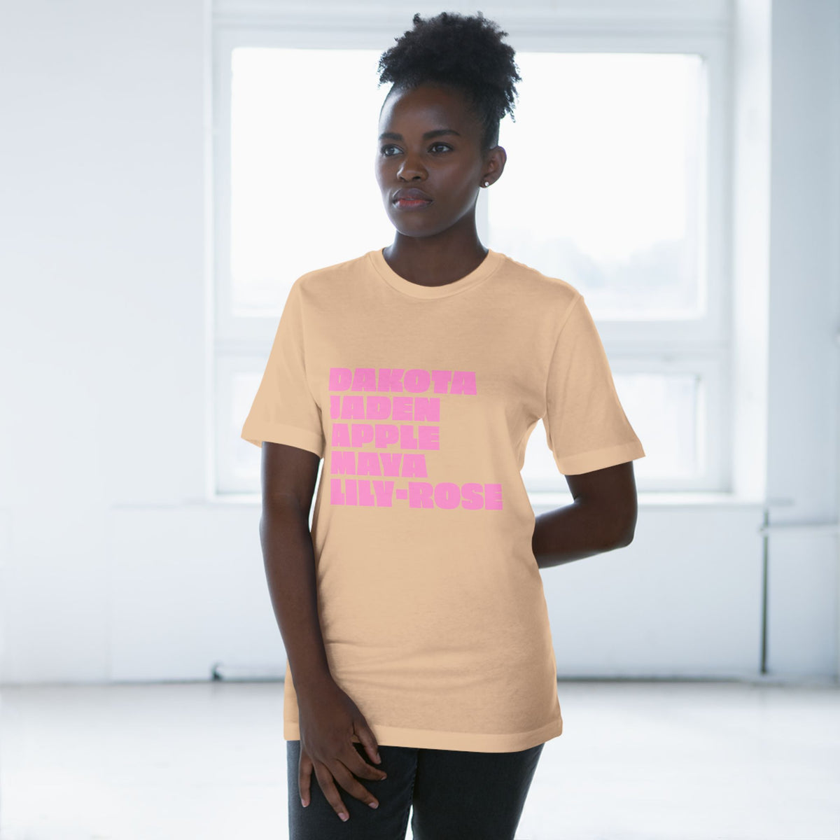 Woman wearing tan Nepo Babies List T-shirt with pink lettering