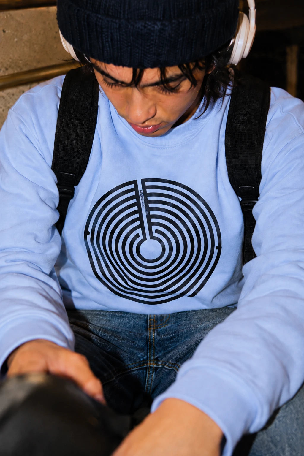 Young man wearing a baby blue Nepo anti-nepotism maze sweatshirt with beanie and headphones.