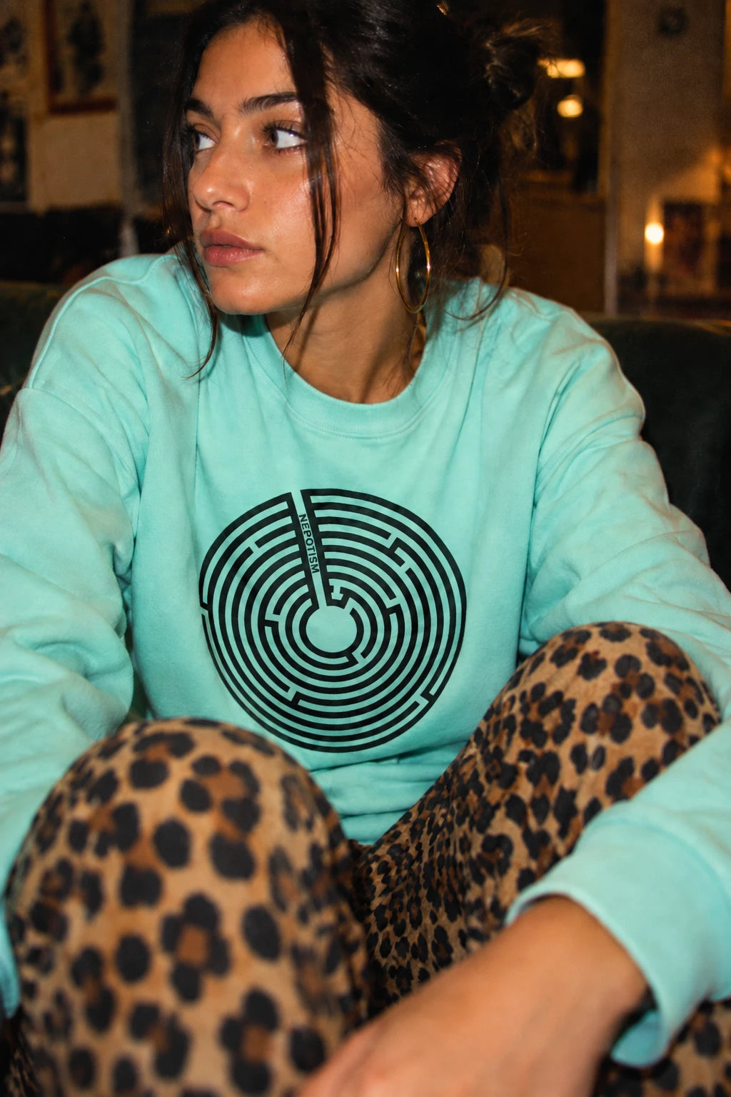 Woman wearing a mint green Nepo anti-nepotism maze sweatshirt in a candid lifestyle scene.