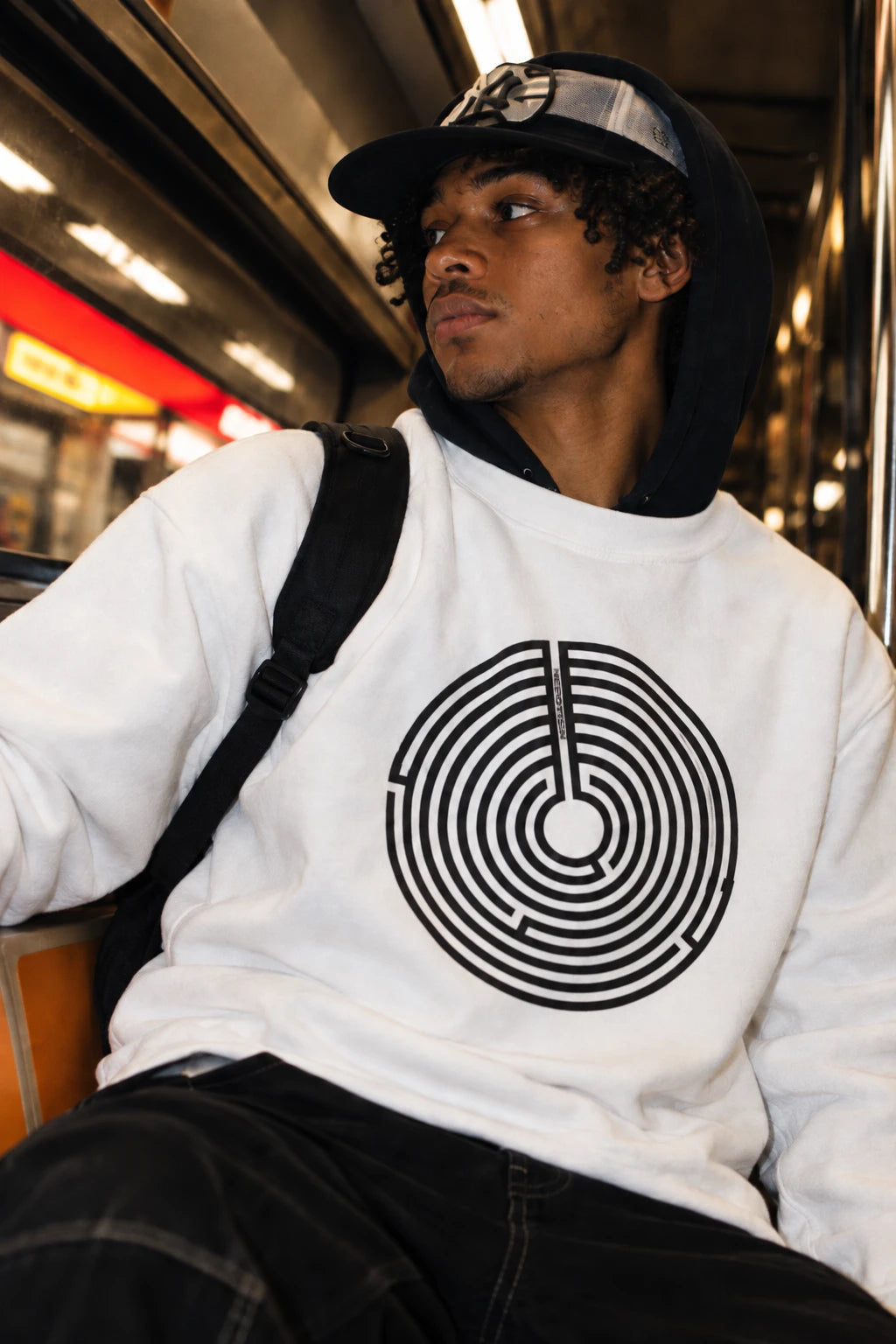 Young man wearing a white Nepo anti-nepotism maze sweatshirt on the subway.