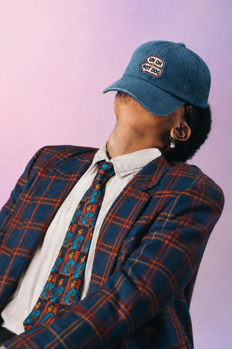 Retro editorial portrait of a man wearing the Nick Rhodes Unisex Necktie with a blue and red plaid blazer against a soft pink background.