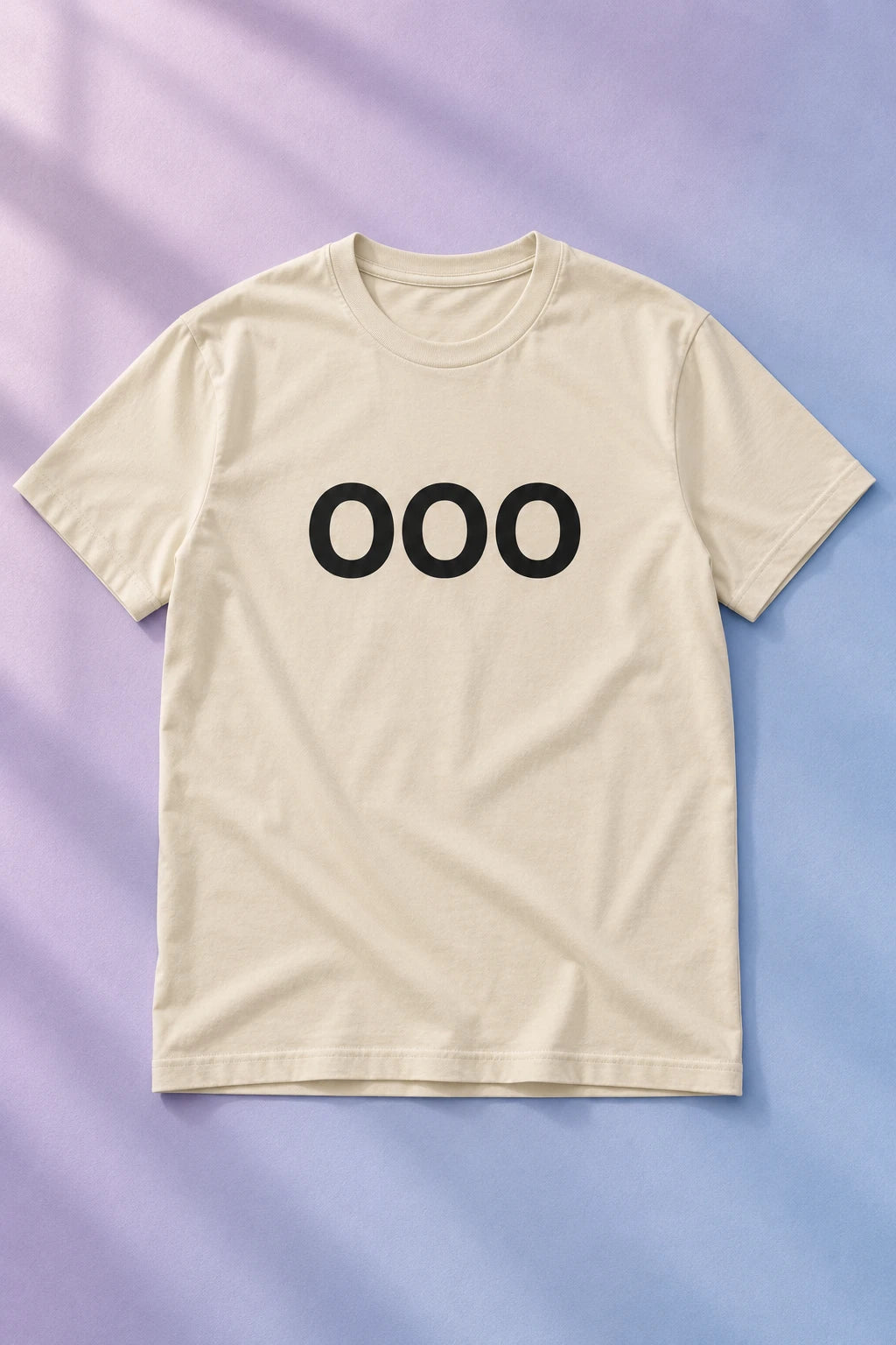 Cream OOO T-shirt laid flat on a pastel lilac and blue background.