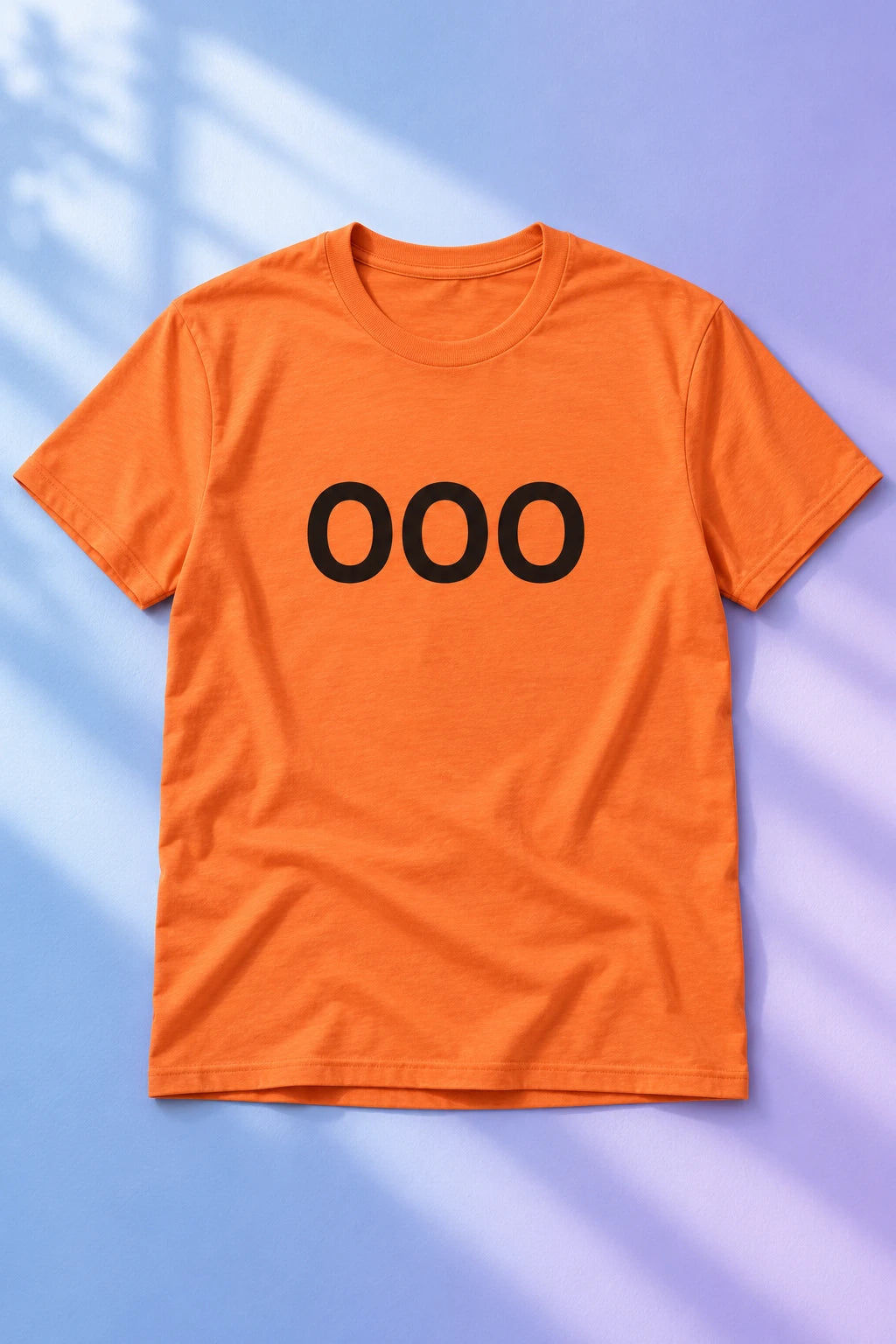 Orange OOO T-shirt laid flat on a pastel blue and lavender background.