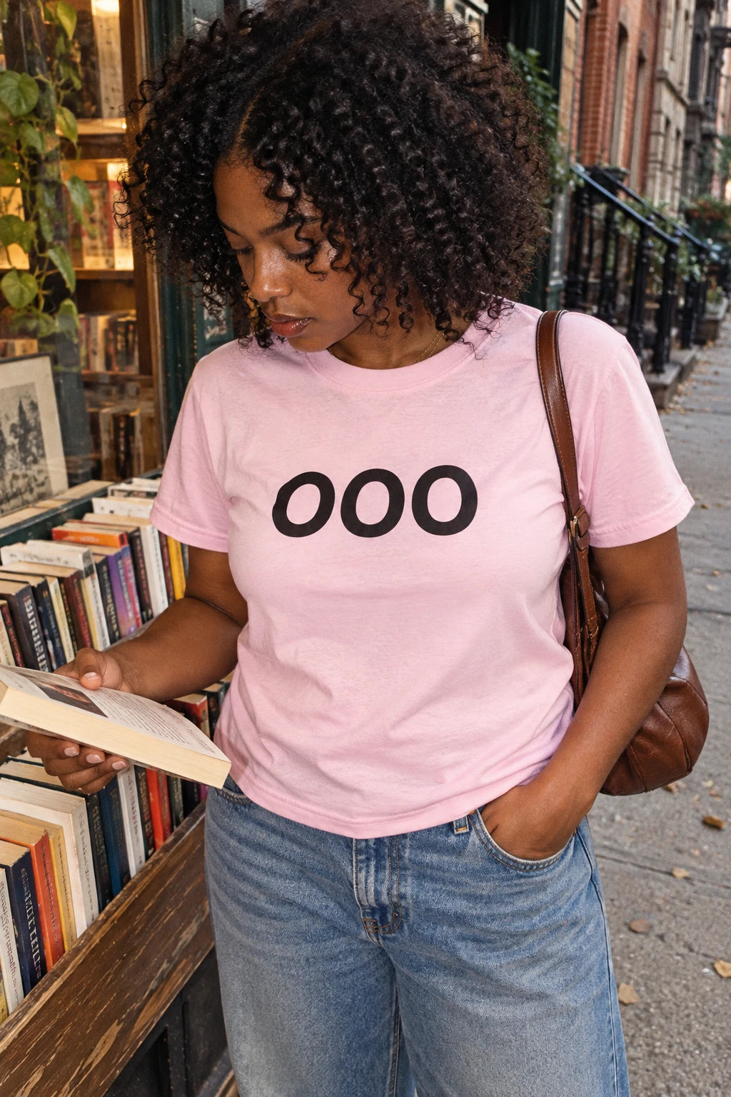 Woman wearing a pink OOO T-shirt while browsing books outside a neighborhood bookstore.