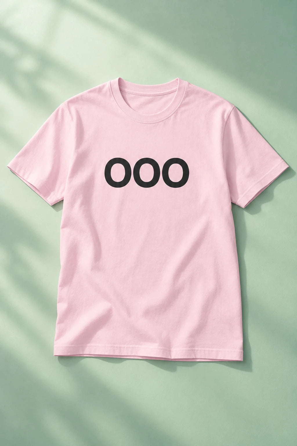 Pink OOO T-shirt laid flat on a soft mint-green background with gentle shadows.