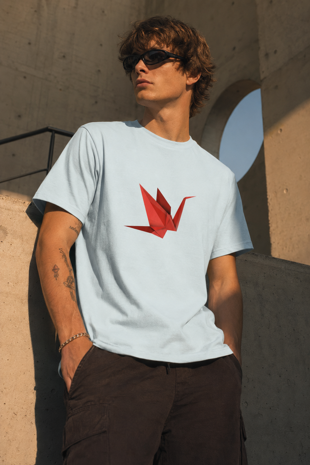 Young man wearing the Origami Crane T-Shirt featuring a red paper crane graphic in a modern architectural editorial photography scene.
