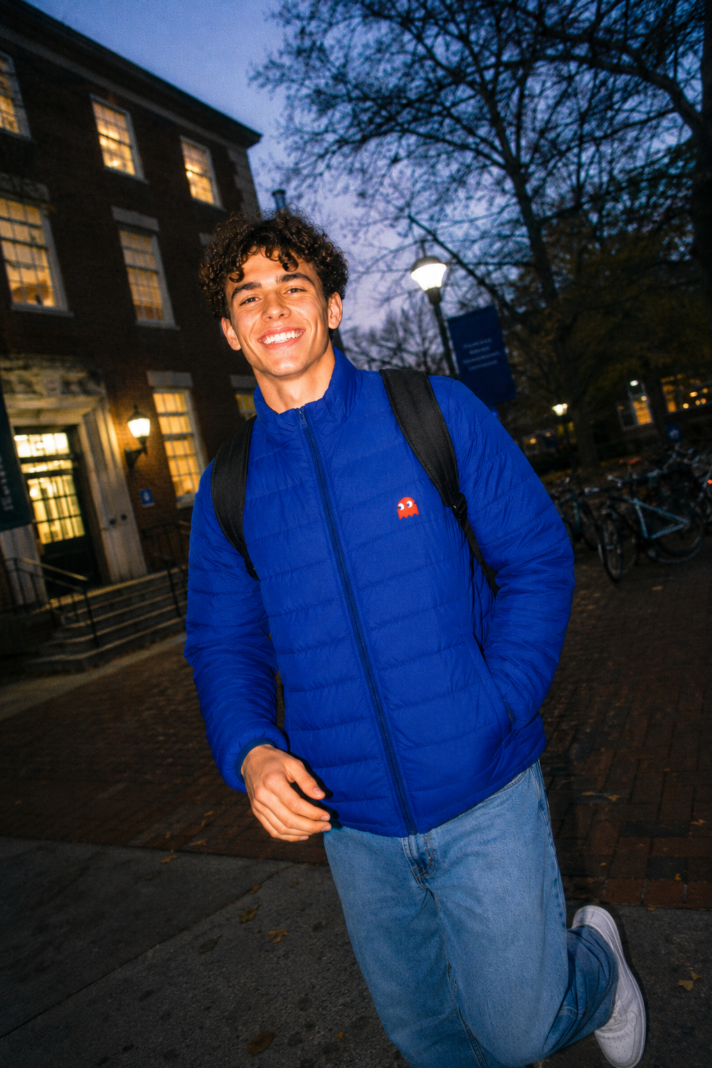 Gen Z student wearing the Pac-Man Blinky Ghost men’s blue puffer jacket on a college campus with a disposable camera aesthetic.