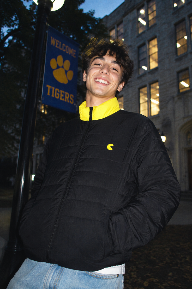 Gen Z college student wearing the Pac-Man men’s black and yellow puffer jacket in a dramatic campus lifestyle shot.