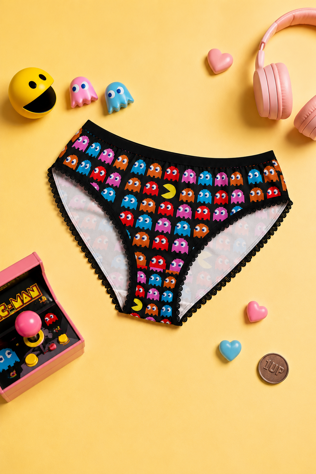 Pac-Man women’s briefs with colorful ghost print and black lace trim styled on a yellow gaming flat lay
