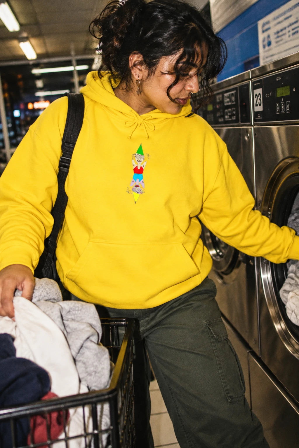 Woman wearing the yellow Party Favor graphic hoodie in an urban laundroma