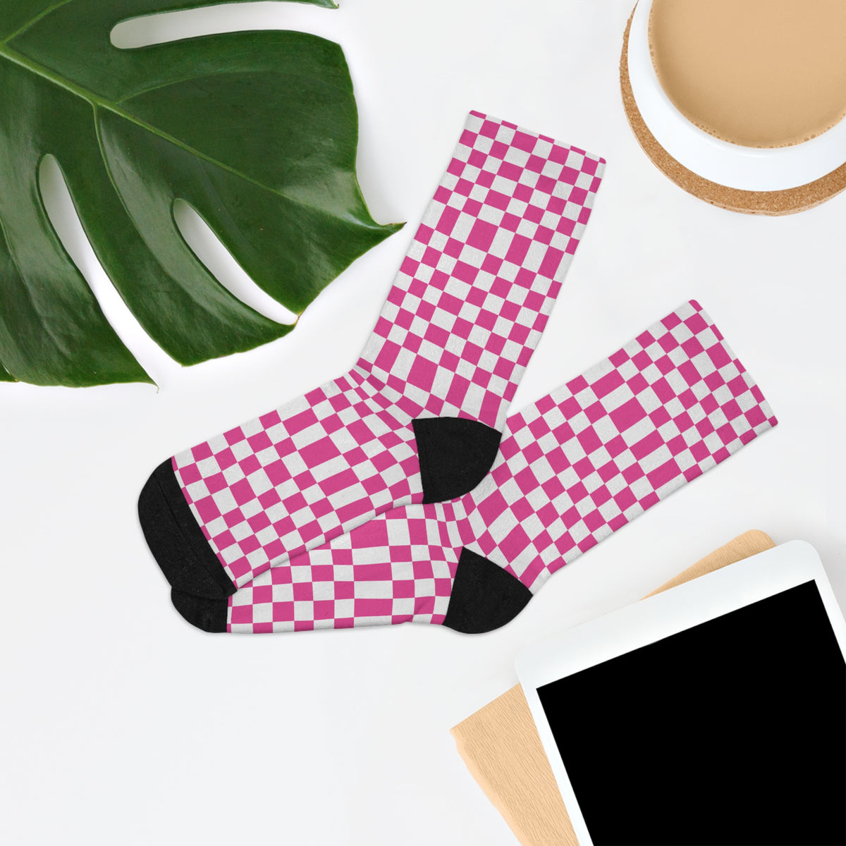 Pink checkerboard crew socks in an editorial flat lay with greenery and desk accessories.