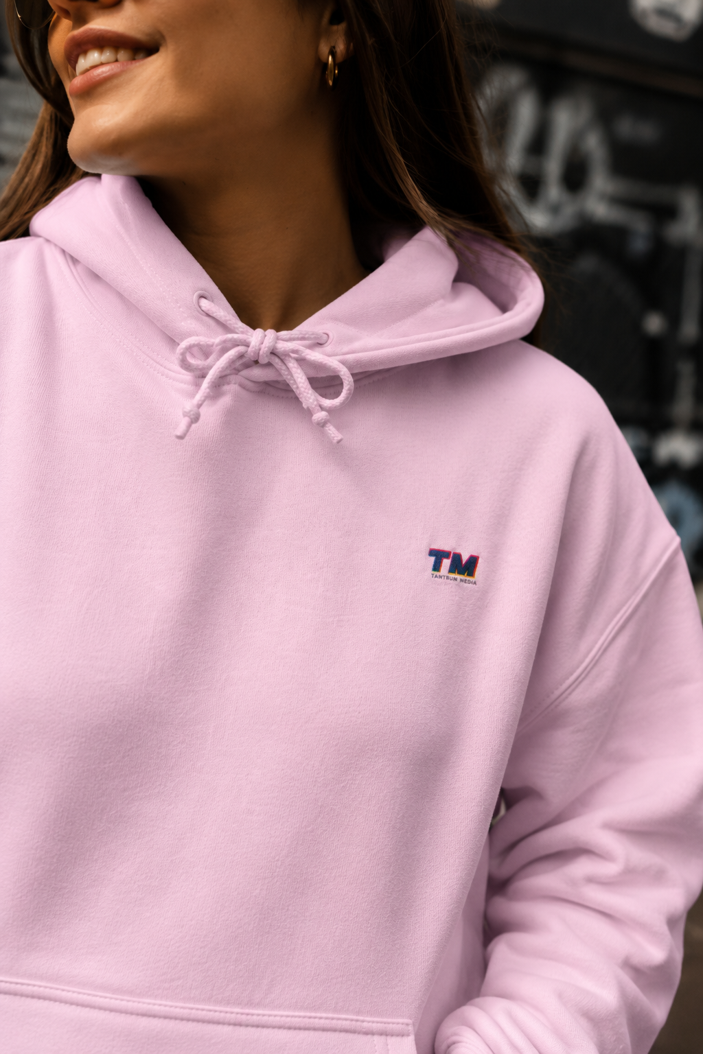 Close-up editorial detail of the Tantrum Media EcoSmart pink hoodie showing its soft fleece fabric and embroidered logo.