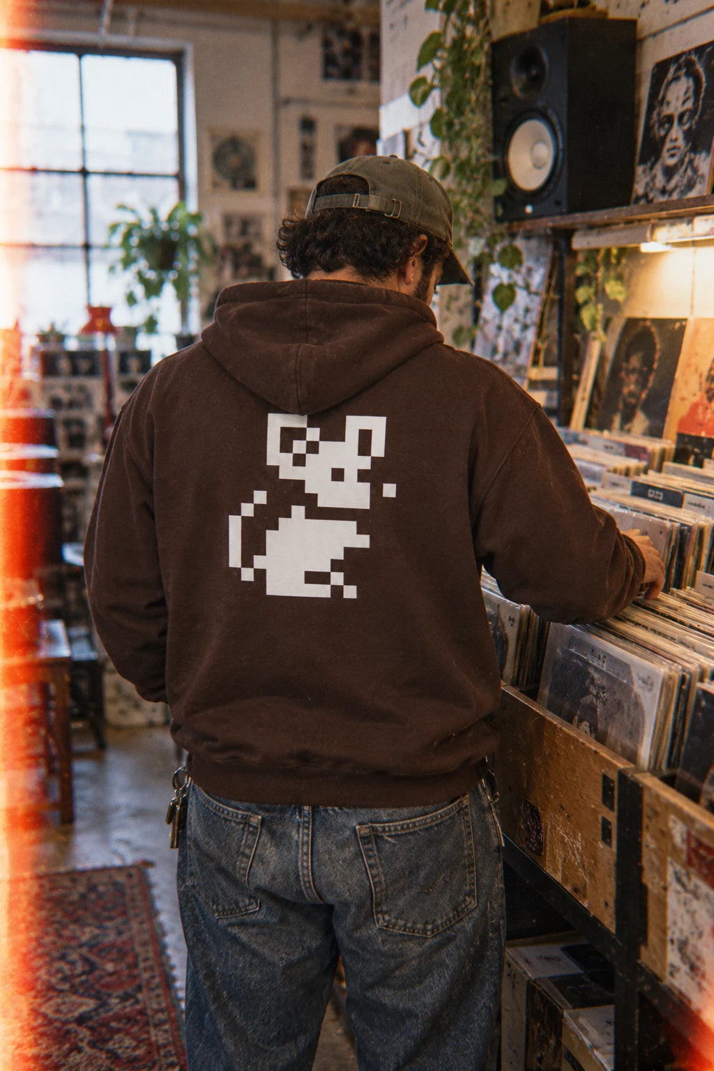Brown Pixel Mouse Zip Hoodie worn from the back while browsing a record store
