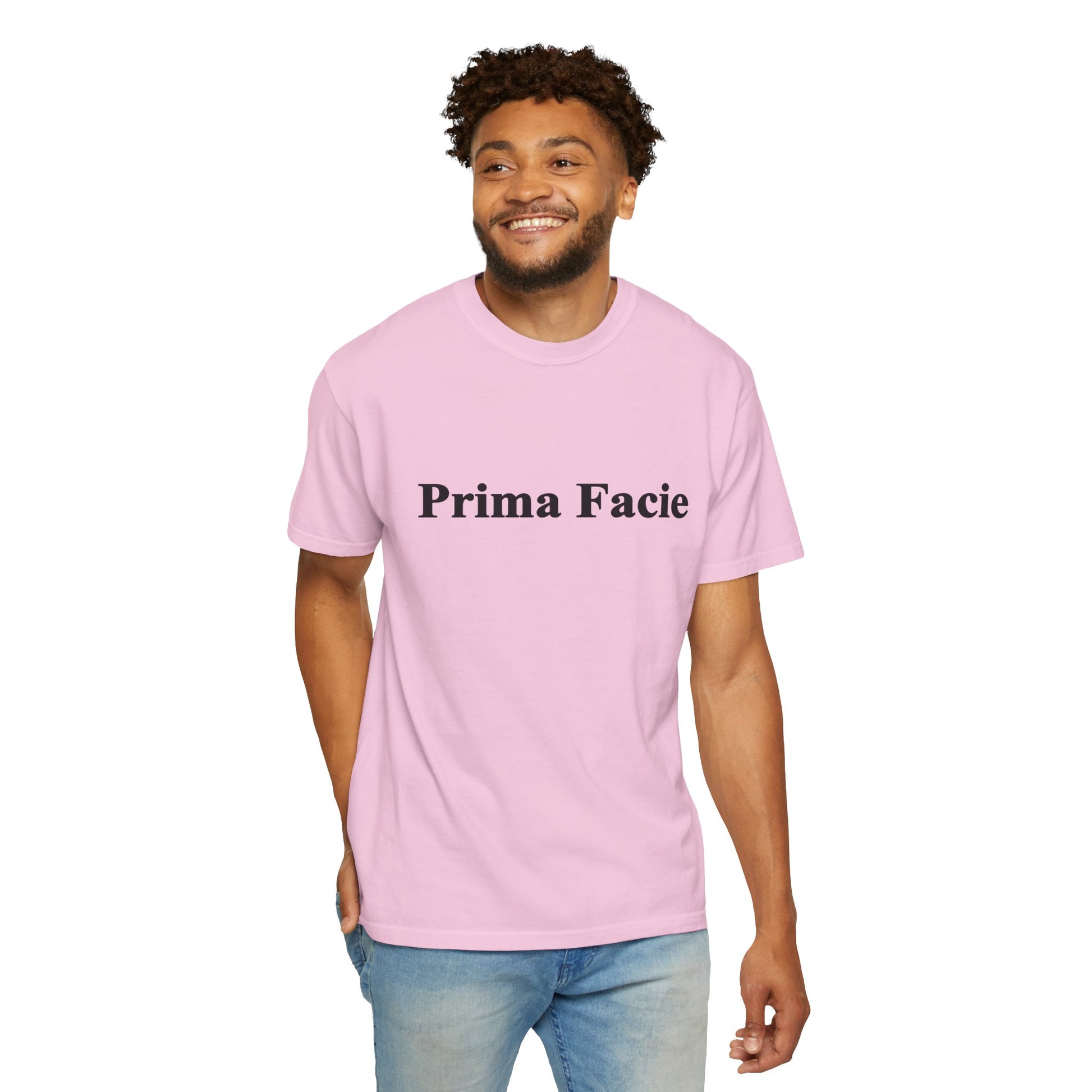 Young male model wearing a light pink Prima Facie unisex graphic T-shirt in a casual studio portrait.