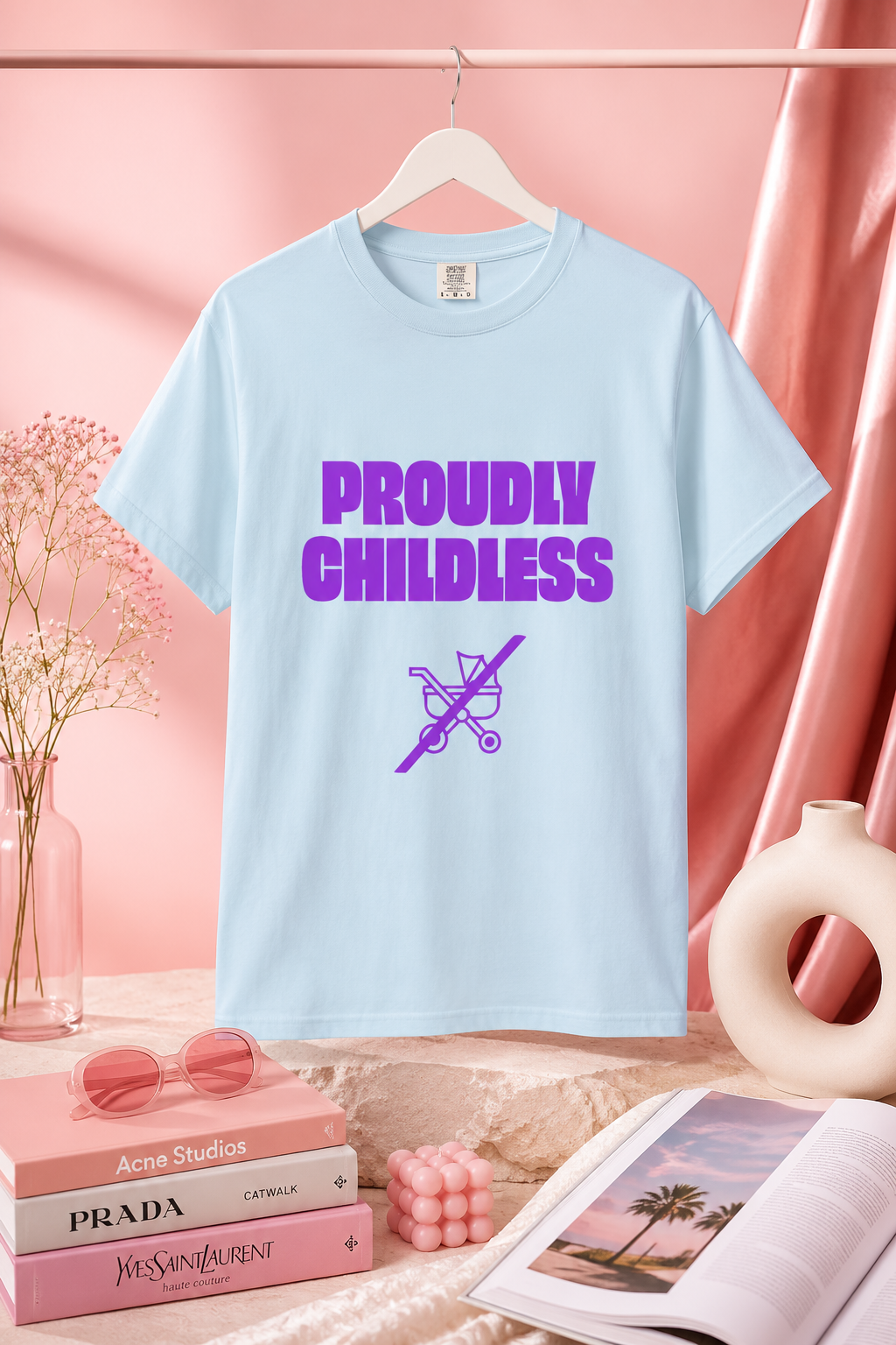 Light blue Proudly Childless graphic T-shirt displayed in a pastel pink editorial setting