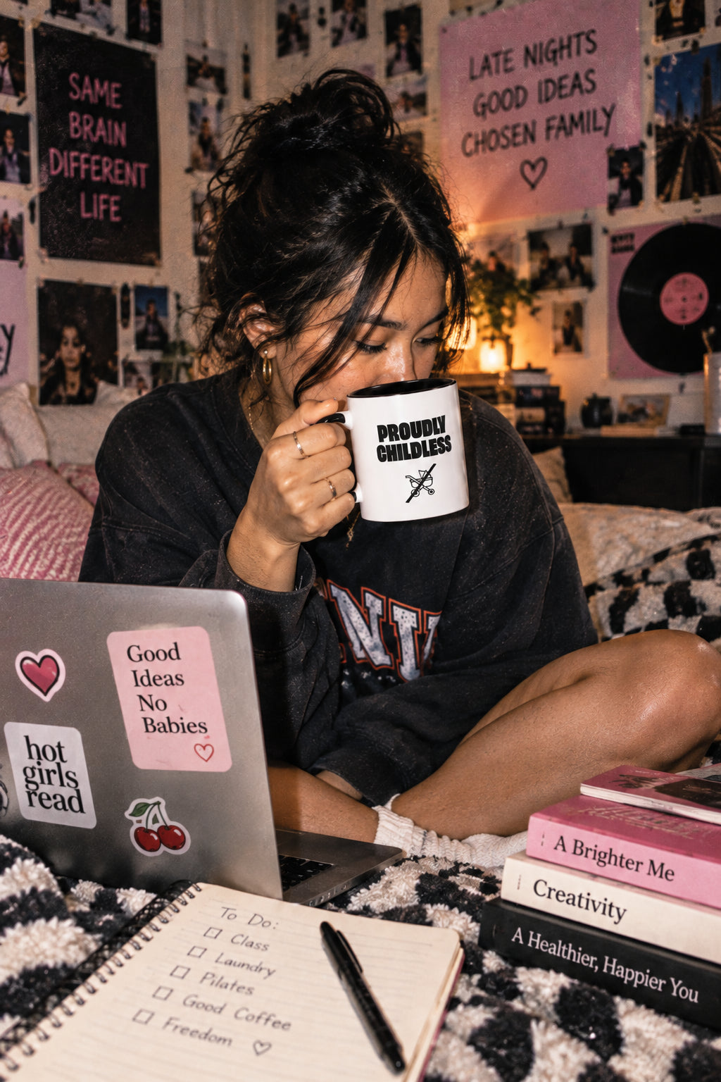 Young woman drinking from the black Proudly Childless Mug while studying in a college dorm