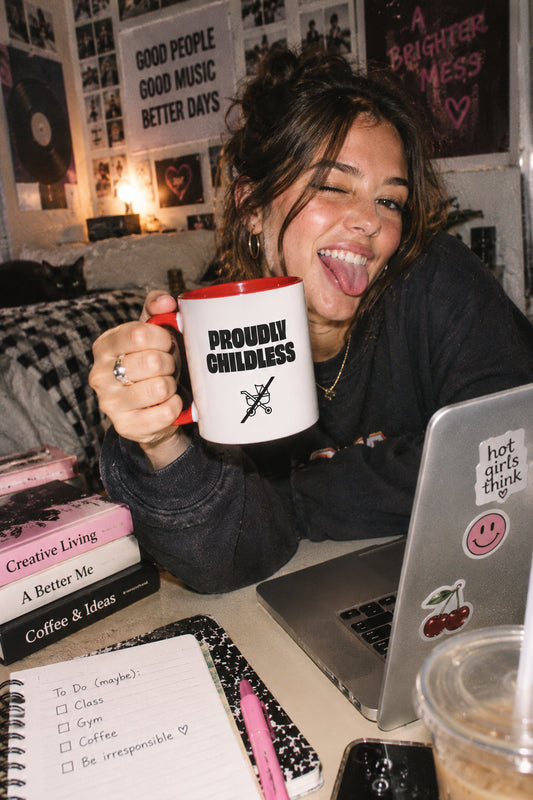 Young woman holding the Proudly Childless Mug in a casual college dorm room